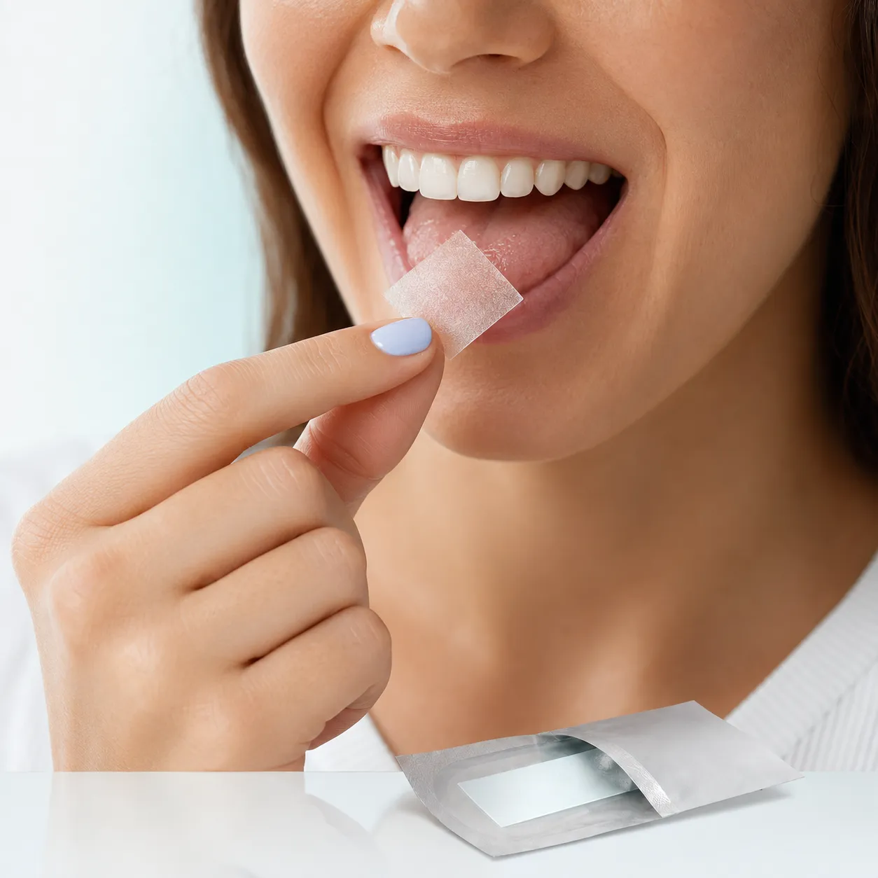 A person placing a thin oral strip on their tongue, with an open foil sachet in the foreground